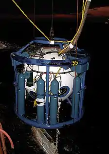 A US Navy Diver transfer capsule, or dry bell. This is a spherical steel chamber in a framework supporting several compressed gas cylinders, which has a bottom-access hatch which allows divers access while underwater. The sealed chamber can be used to transfer divers from a hyperbaric habitat at the surface to the underwater work-site, and can also be used as a decompression chamber if necessary